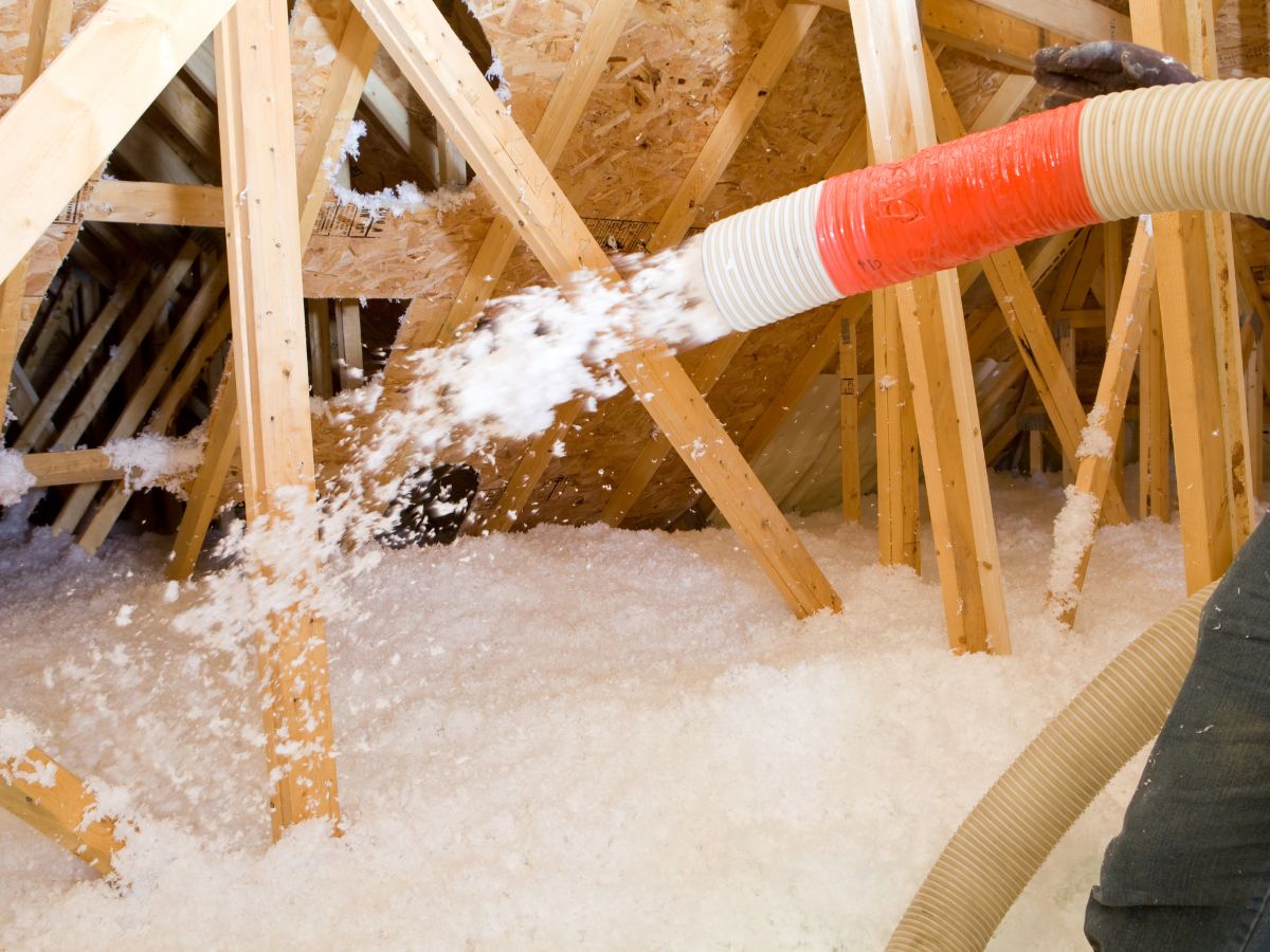 A man operates a vacuum to extract insulation from a roof, demonstrating a home improvement task.