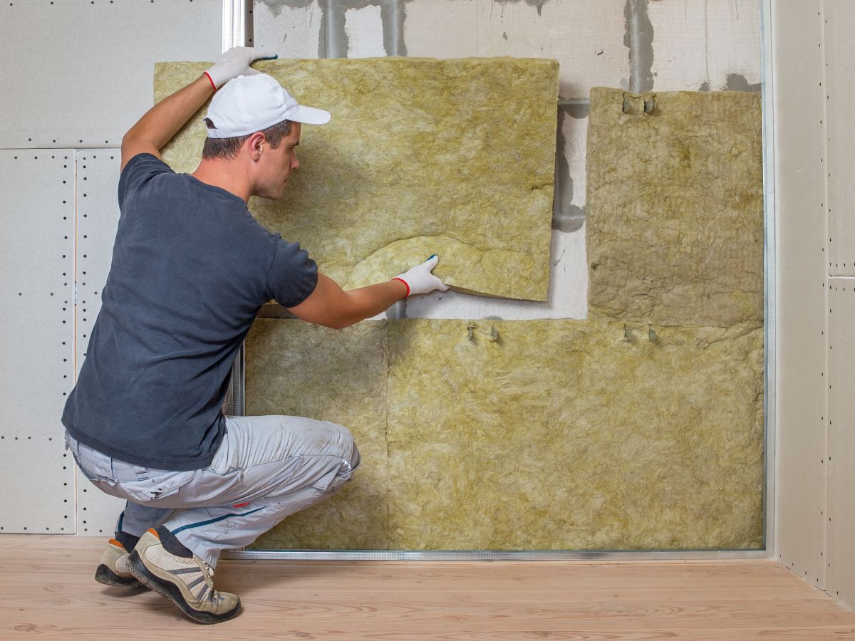A man installs insulation in a room, carefully placing materials between the wall studs for energy efficiency.
