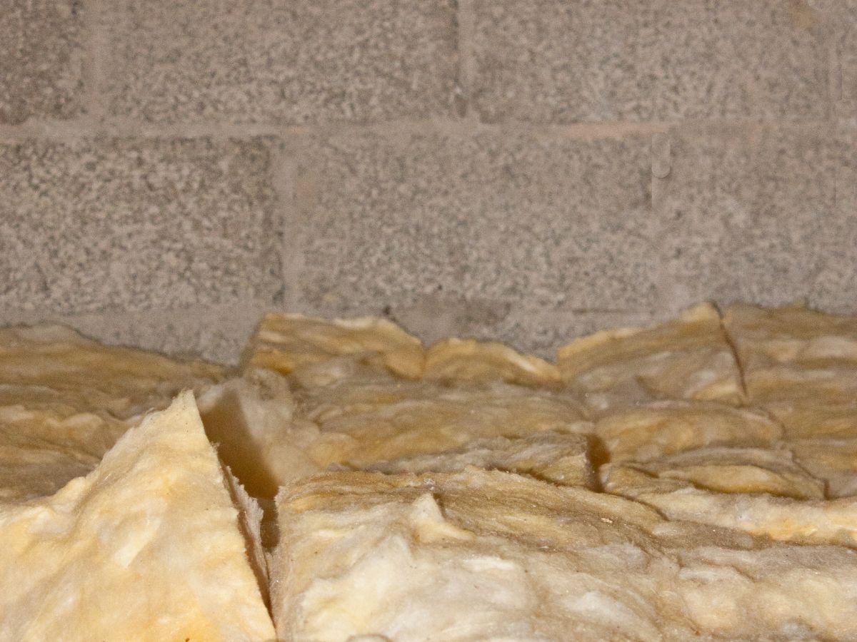 Insulation material is stacked on the floor against a backdrop of a rustic brick wall in an indoor setting.