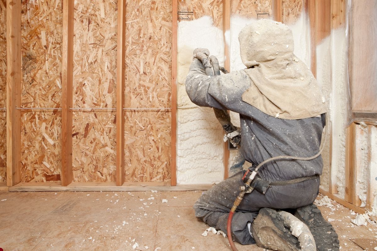 A man in a hard hat and jacket paints a wall, representing an insulation service in progress.
