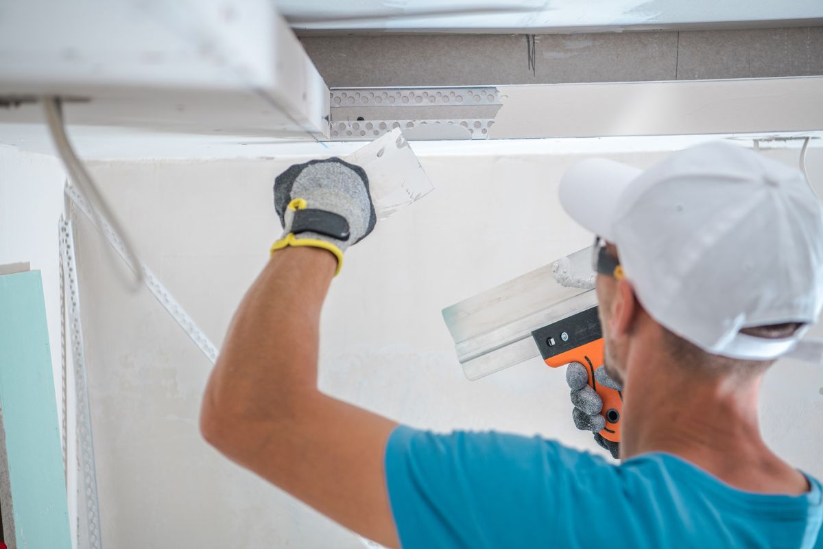  A man operates a power tool to paint a ceiling as part of an insulation service project.