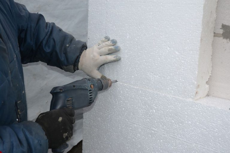 A man operates a drill, installing insulation by drilling into a wall.