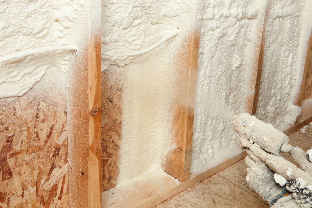 A man applying spray foam insulation to a wall, demonstrating the process of removing old insulation.