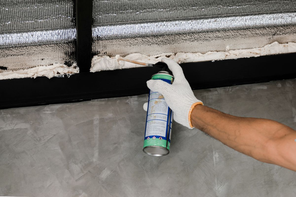 A person spraying a cleaning solution on a wall to remove spray foam insulation.