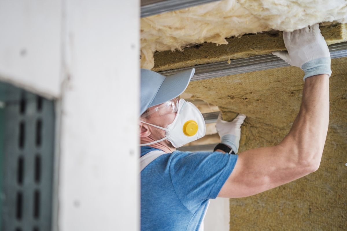 A man wearing a blue shirt and white gloves installs insulation on a roof, focusing on roof types and insulation techniques.