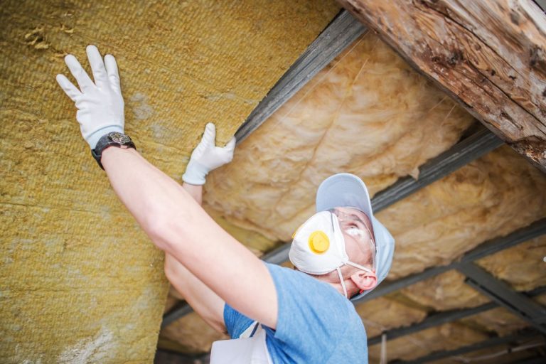 A man in a mask and gloves installs insulation on a roof, demonstrating safety and proper technique for roof insulation.